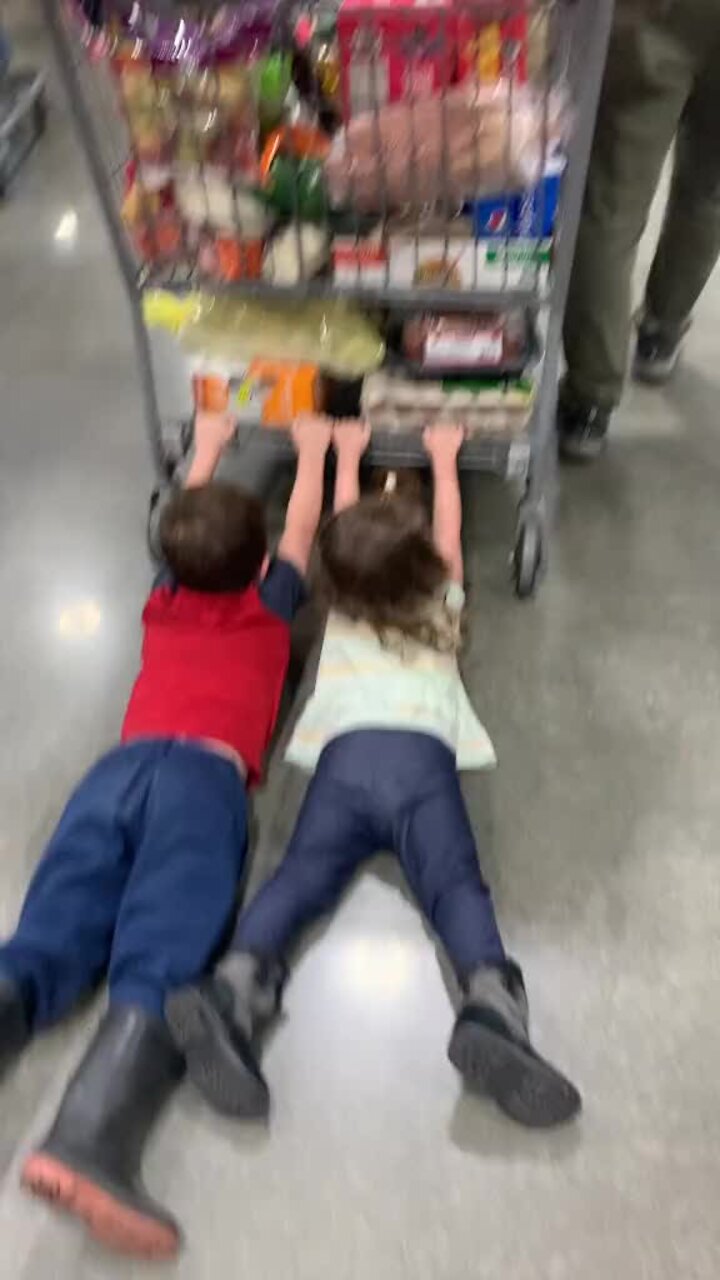 Two kids are pulled by a shopping cart at Costco, being dragged behind ...