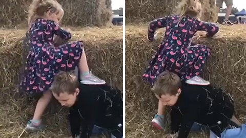 Sweet kid helps his little sister climb onto a tall haystack