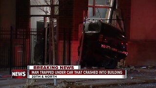 Man trapped under a car after a vehicle strikes building