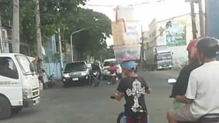 Street vendor carries boxes on head while riding bike