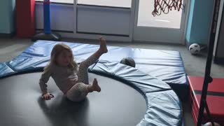 Little girl shoots basketball into hoop while on trampoline and falls back