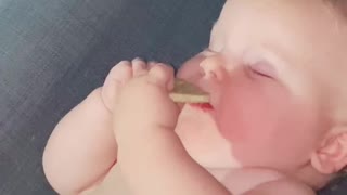 Tired baby eats a cookie while half asleep