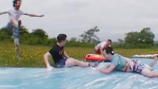 Guy slides off ramp on soap water slide with friends