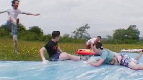 Guy slides off ramp on soap water slide with friends