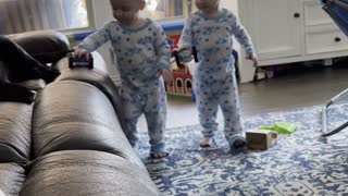 Twin toddlers amused by rolling toy cars on the sofa