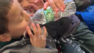 Boy feeds little brother water, squeezes water bottle and splashes his face