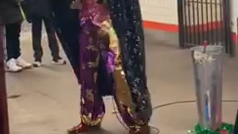 Man in sequin pants and sparkly red vest dances and sings in subway station