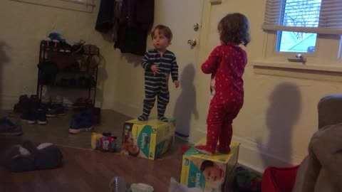 Twins engage in epic debate while standing on diaper boxes